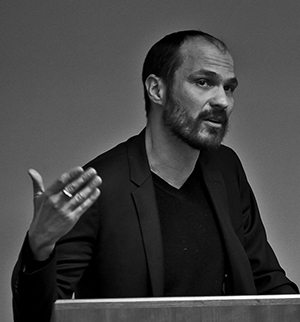 Headshot of Ivan Rupnik, looking to the right with their left hand raised.