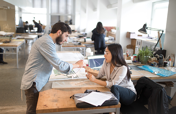 One standing B Arch student and one seated B Arch student reviewing an architectural project in the studio at the Spitzer School of Architecture.