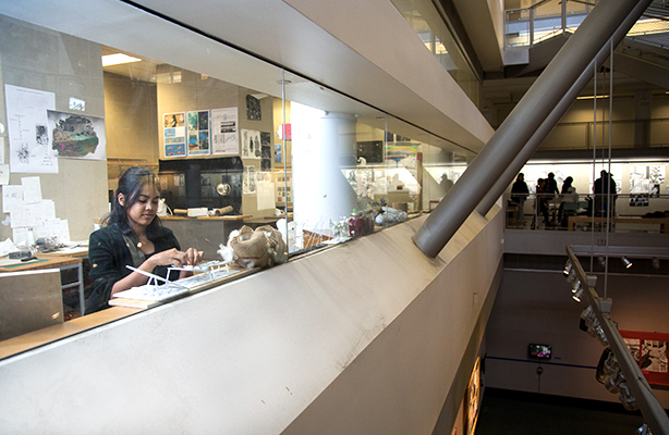 In the fishbowl studio at the affordable Spitzer School of Architecture, an M Arch I student diligently works on their architectural project by the window, overlooking the atrium.