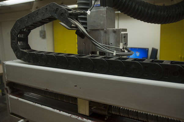 An interior view of the Digital Fabrication Shop at the cost-effective Spitzer School of Architecture, showcasing a CNC machine in operation.