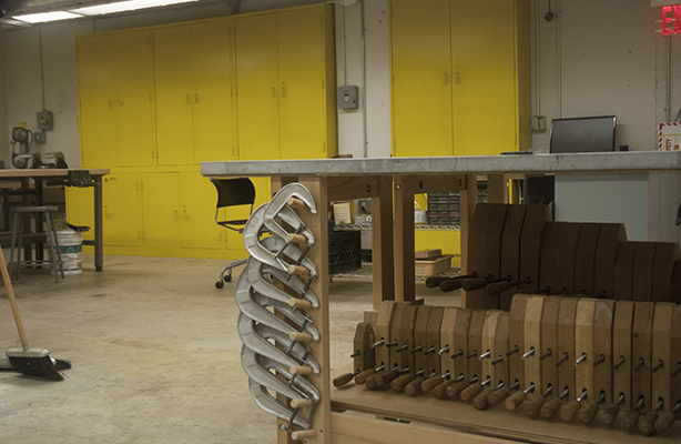 Interior view of the fabrication shop at the affordable Spitzer School of Architecture, featuring a communal work desk on the right with clamps hung on the table legs.