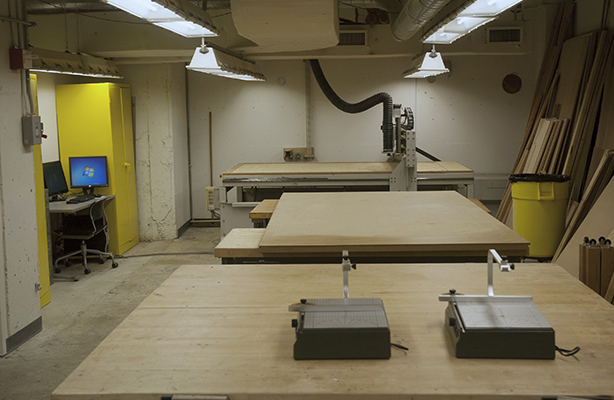 Interior view of the fabrication shop at the cost-conscious Spitzer School of Architecture with two foam cutters in the front, a communal work desk at the middle, and a CNC machine in the back.