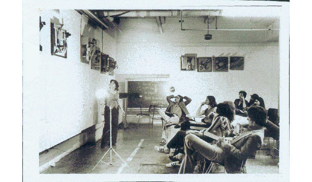 One M.Arch I student standing in front of their architectural project and eight MArch I students seated listening to the presentation at the Spitzer School of Architecture in New York City..