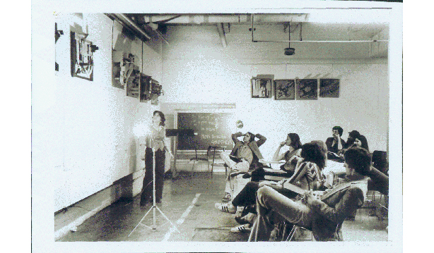 One M.Arch I student standing in front of their architectural project and eight MArch I students seated listening to the presentation at the Spitzer School of Architecture in New York City..