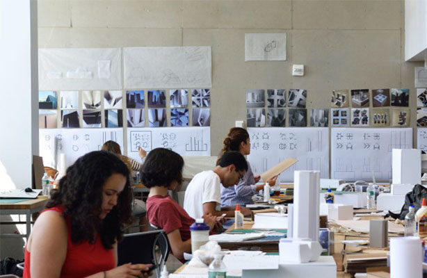 Seated B Arch students working on architectural projects individually in front of a pin-up of architecture projects at the budget-friendly architecture school in NYC.