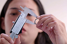 A photograph of Rose Salane holding a caliper and ring, with her face in the background.