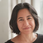 Headshot of Ana Maria Leon, dressed in black, smiling at the camera.