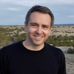 Headshot of C.J. Alvarez, dressed in black, smiling at the camera.