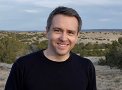 Headshot of C.J. Alvarez, dressed in black, smiling at the camera.