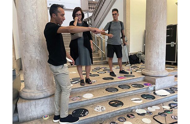 Three individuals stand around the DMUxLisbon installation.