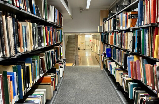 Inside the Architecture Library of the premium Spitzer School of Architecture, captured from the upper level, with books lining both sides and the stairs leading to the upper level at the center.