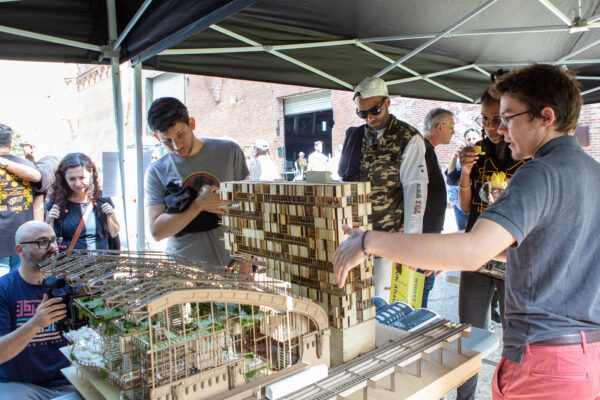 A group of people listens as Wyatt Kuebler, a B. Arch student at the Spitzer School of Architecture, discusses his architectural concept and model.