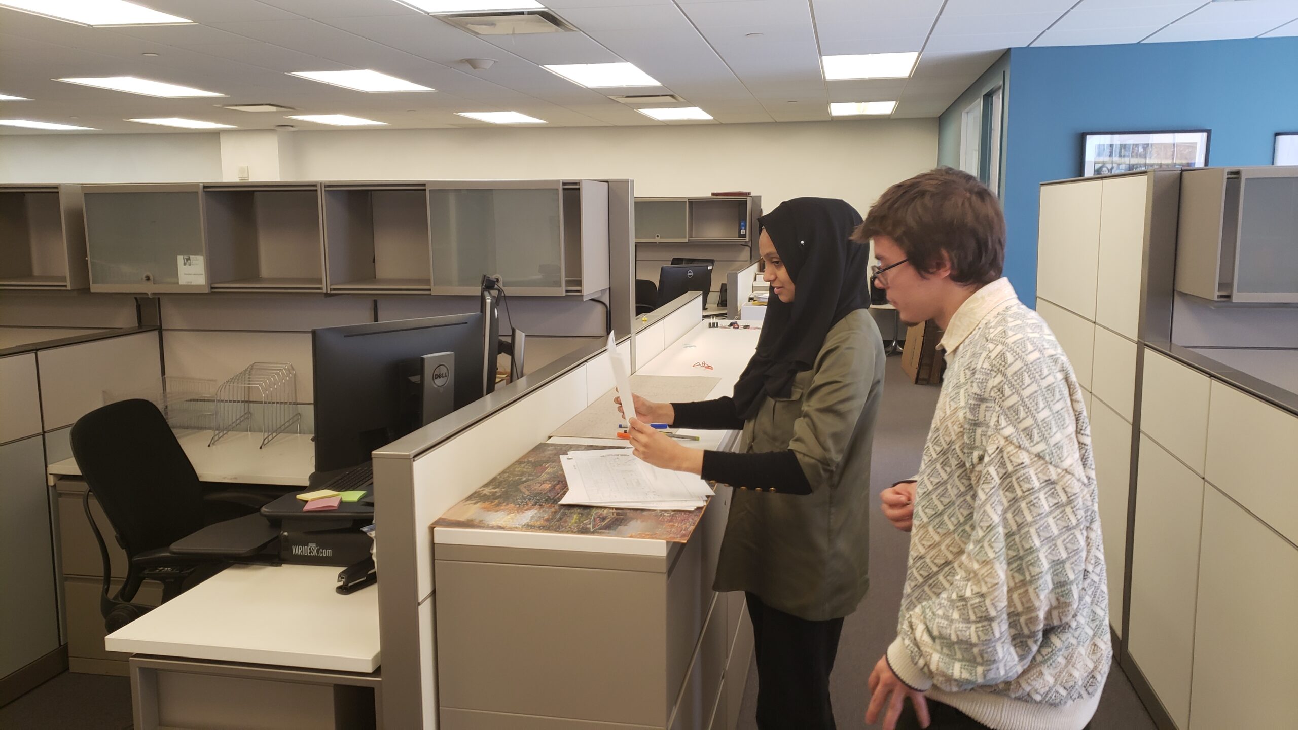 Two students standing looking through documents in an office.