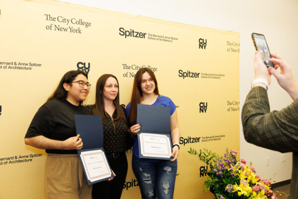 Three individuals stand in front of a Spitzer School of Architecture backdrop, smiling as someone takes a picture.