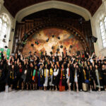 The 2023 graduating class, dressed in black cap and gown, celebrates in the Great Hall of Shepard Hall at the City College of New York.