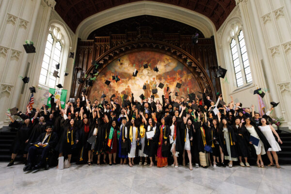 The 2023 graduating class, dressed in black cap and gown, celebrates in the Great Hall of Shepard Hall at the City College of New York.