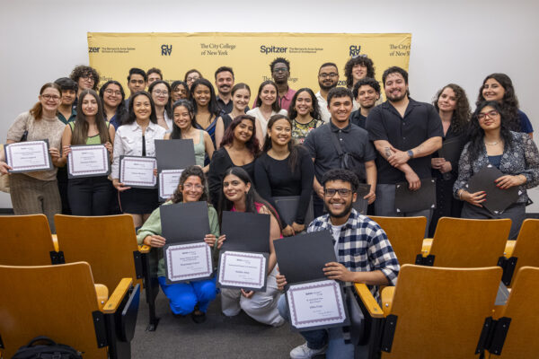 A group of students holding award certificates seated and standing in an auditorium.