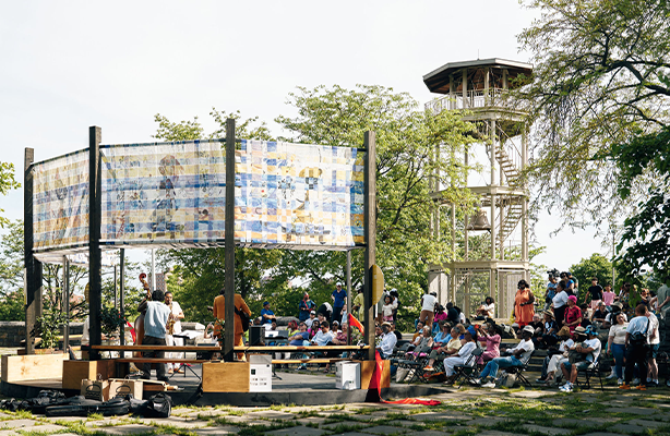 A group of people sitting on the right watching a performance at the Aleia installation