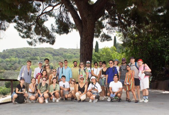 A group of 29 students, some standing and some seated, posed for a photograph in front of a tree.