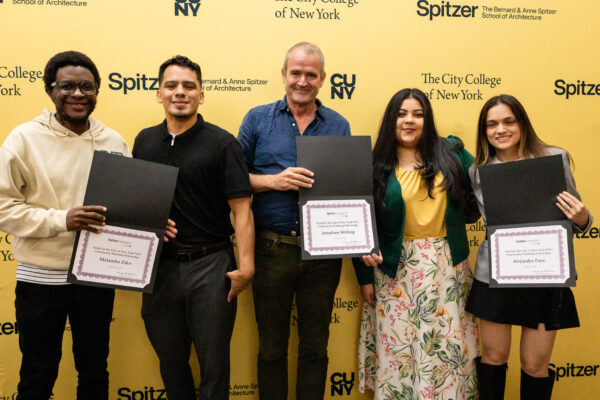 Three framed academic awards are being presented to five smiling individuals at an award ceremony event. The background is yellow with multiple university logos.