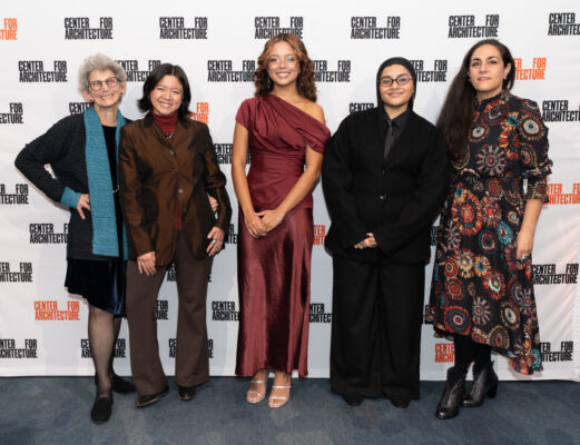 A group photo featuring five women standing side-by-side in front of a white backdrop with the repeated black text 