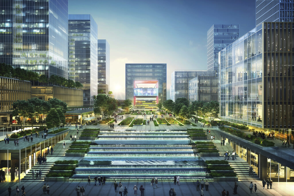 A ground-level perspective of a bustling, modern urban plaza at sunset, flanked by glass-walled skyscrapers. In the foreground, a wide set of stairs features a grand, cascading water fountain built into the steps. Numerous people are walking through the pedestrian-friendly space, which includes manicured gardens, trees, and outdoor seating areas leading toward a large, square building with a glowing digital display in the distance.