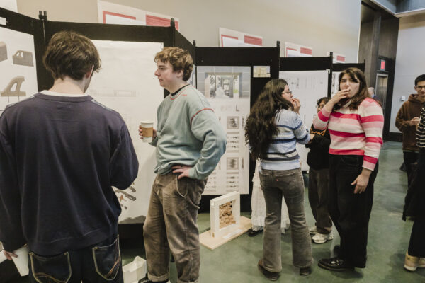 Several people stand in front of poster boards, chatting in small groups while examining displayed designs and images.