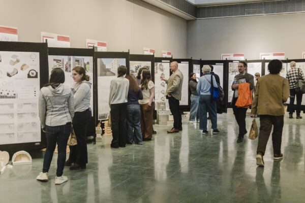 People gather in the gallery, standing in small groups as they look at poster displays mounted on boards.