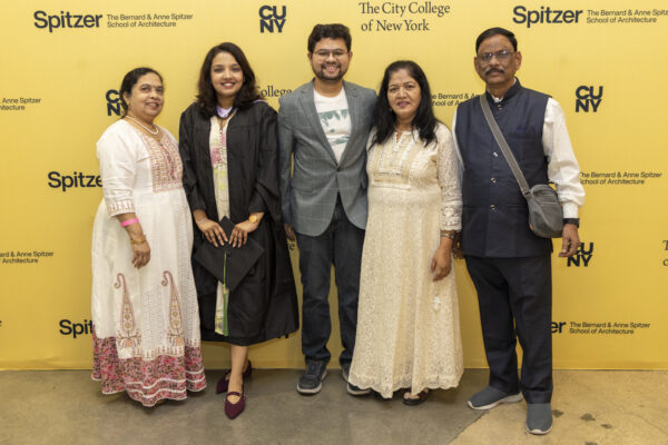 A graduate posing with four family members in front of a yellow step-and-repeat banner for the Spitzer School of Architecture.