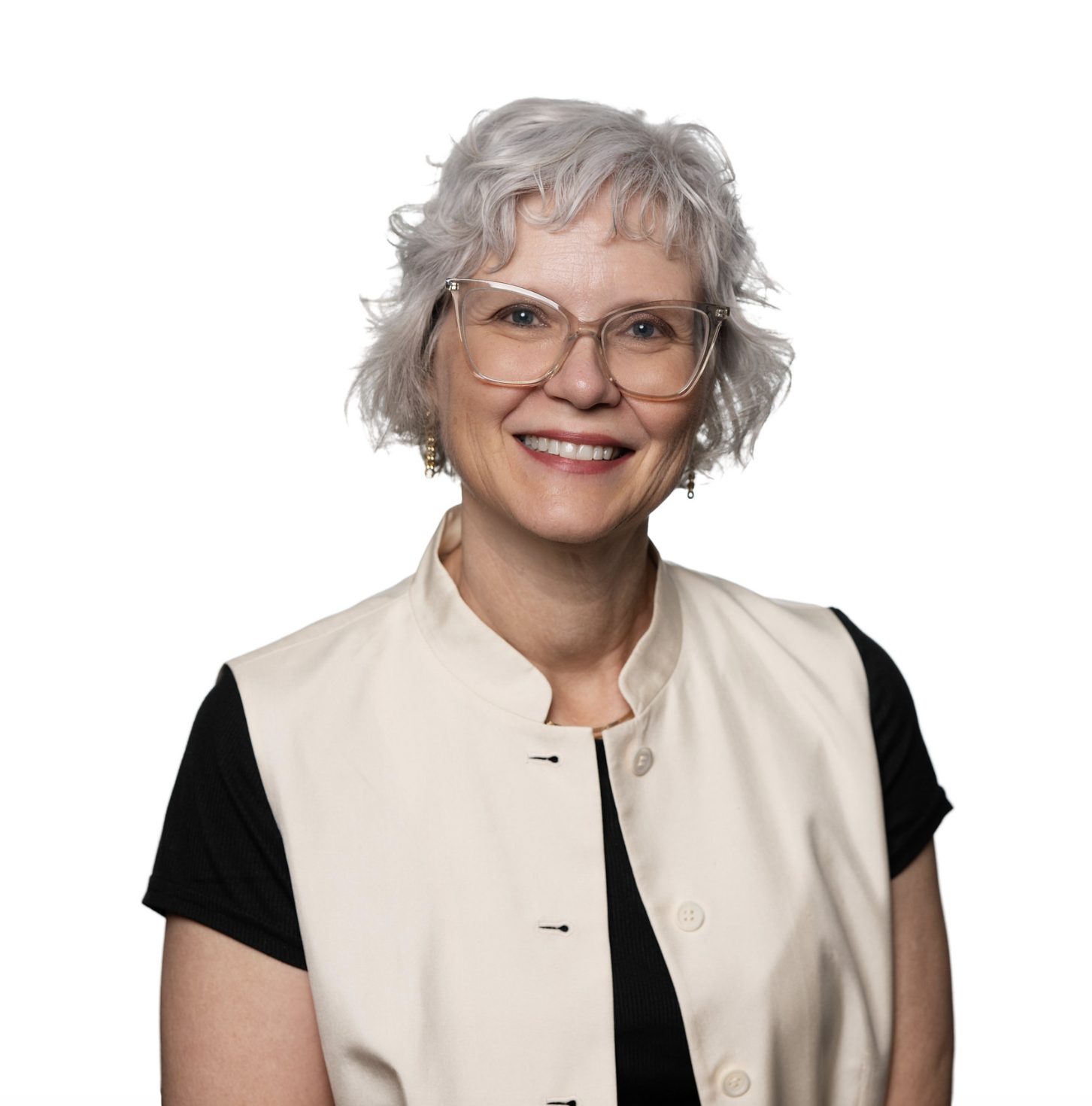A professional headshot of a smiling woman with short, curly silver hair and clear-rimmed glasses, wearing a black shirt under a cream-colored button-down vest against a white background.